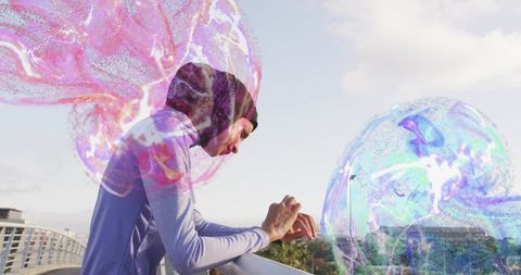 Female athlete wearing dark headscarf leaning on bridge railing with holographic jellyfish