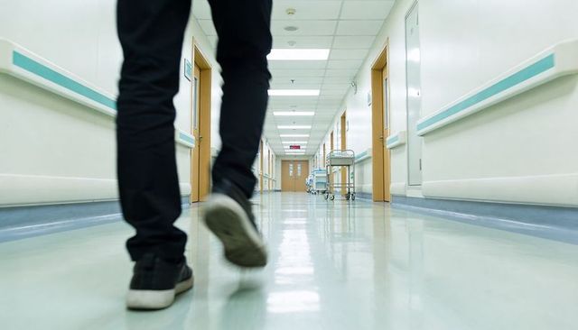 Person walking down hospital corridor wearing sneakers and black pants with strong perspective