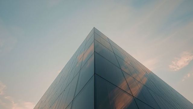 Rising glass facade pointing at pastel sky with cloud reflections and minimalist geometric symmetry