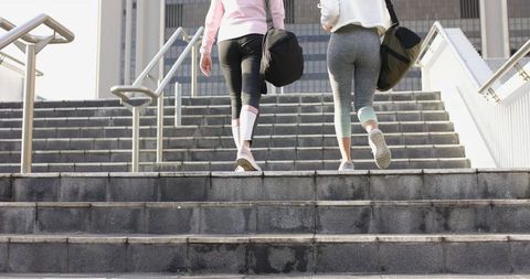 Two women walking up urban stairs carrying gym bags in activewear and leggings