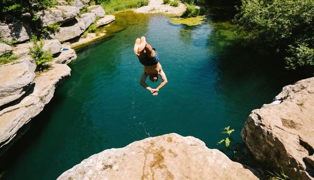 Cliff diver flipping into emerald swimming hole from sunlit rock ledge summer adventure