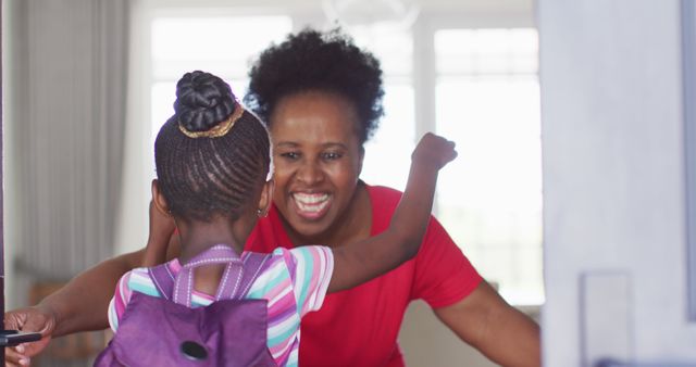 Image of african american granddaughter with schoolbag coming home and hugging happy grandmother. Childhood, family and domestic life.