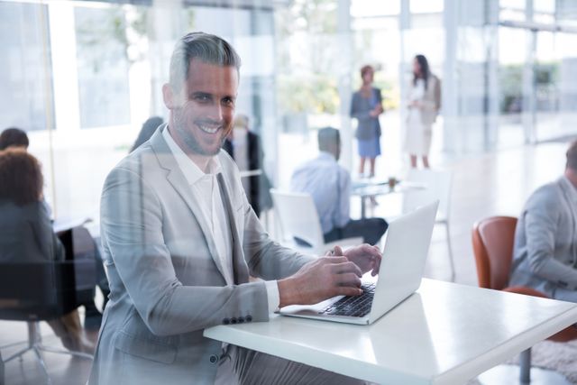 Businessman smiling while using laptop in a modern office environment. Ideal for corporate websites, business presentations, and marketing materials showcasing professional workspaces, teamwork, and productivity.