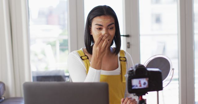 Young woman is applying skincare product while recording a vlog about her beauty routine in a well-lit room. Ideal for content about beauty, skincare tutorials, lifestyle vlogging, and influencer marketing.