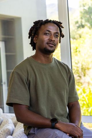 Calm african american man relaxing on sofa by sunlit window in olive shirt and smartwatch