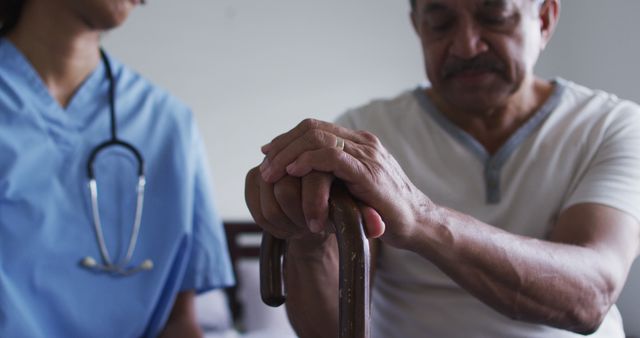 Elderly man holding walking cane receiving help from nurse. Elder care, medical assistance. Useful for healthcare articles, senior care brochure, patient care resources, and medical training materials.