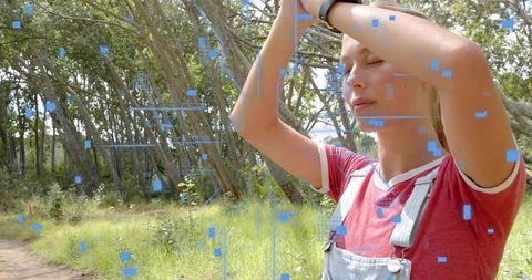 Young woman standing in sunlit woodland touching brow with futuristic blue ar overlays