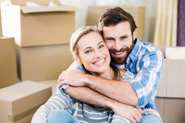This image shows a happy couple embracing each other in their new home surrounded by moving boxes. It is perfect for use in content related to moving, relocation, new beginnings, homeownership, and family bonding. Ideal for real estate websites, moving company advertisements, and lifestyle blogs.