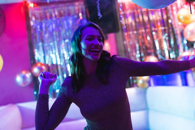 Woman enjoying herself while dancing in a vibrant nightclub with colorful lights and festive decorations. Perfect for use in advertisements for nightlife events, party invitations, or promotional materials for clubs and entertainment venues.