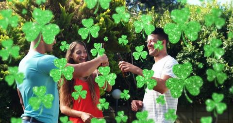 Friends toasting beer in sunlit backyard garden wearing shirts with festive shamrock overlay
