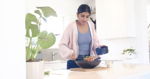 Woman Preparing Fresh Salad in Modern Kitchen with Steel Servers