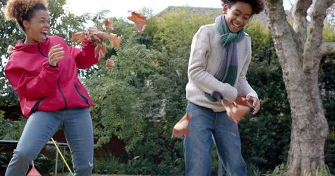 Mother and Son Joyfully Playing in Autumn Leaves in Garden