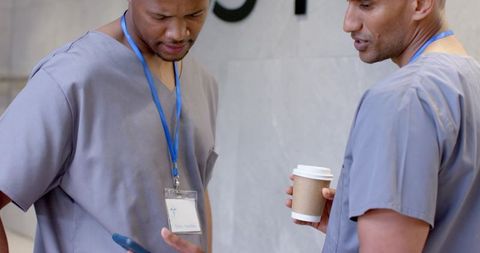 Clinic colleagues in gray scrubs checking phone and holding coffee while wearing id badges