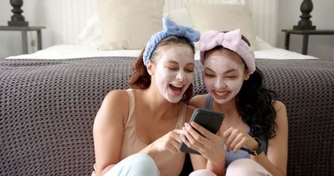Happy Friends Relaxing with Facial Masks and Smartphone
