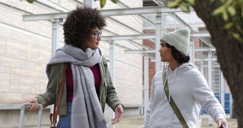 Diverse young women chatting with luggage on campus walkway during overcast day