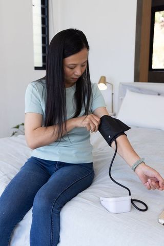 Mature asian woman measuring blood pressure at home with digital monitor and smartwatch