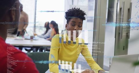 Black woman typing and discussing data at coworking table with digital analytics overlay