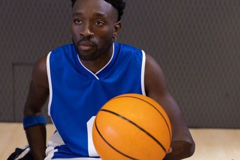 African american basketball player sitting on bench holding basketball wearing blue jersey