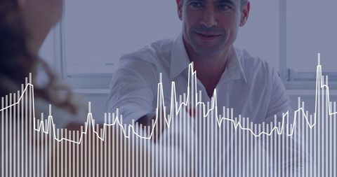 Executive offering handshake across desk with financial charts and analytics overlay