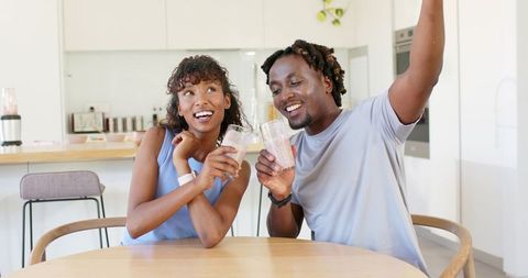 African american couple enjoying pink smoothies at modern kitchen table
