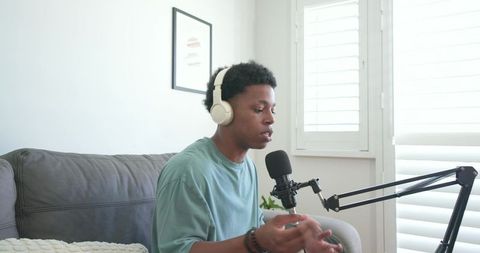 African american man recording podcast at home wearing headphones speaking into microphone