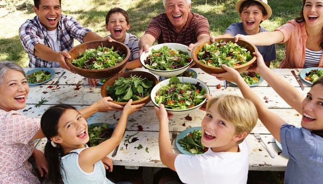 Multigenerational family sharing fresh salads around rustic outdoor picnic table