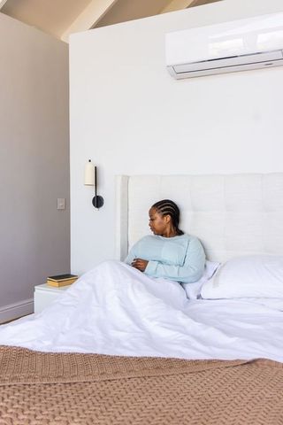 African american woman sitting up in bed in minimalist neutral bedroom with braided hair