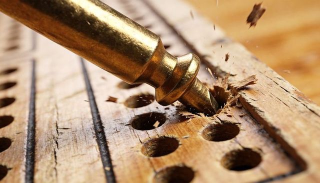 Brass drill bit drilling pilot hole into wooden jig, wood chips flying, carpentry closeup