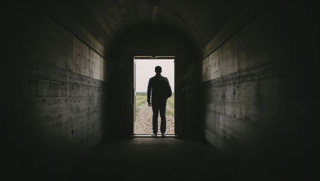 Standing Silhouette Traveler Exiting Dark Tunnel Through Archway Into Lighted Gravel Path