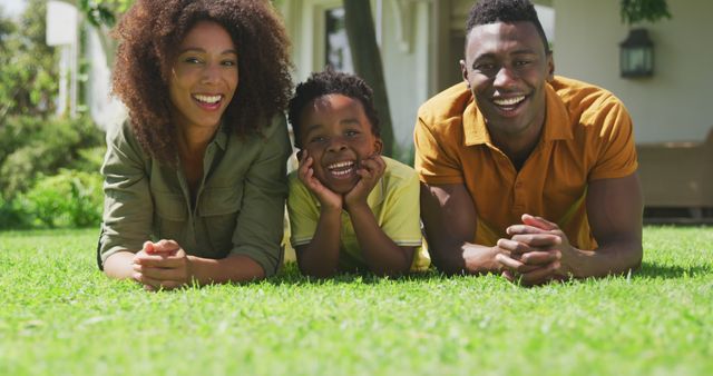 Family enjoys quality time lying on grass in sunny backyard. Perfect for advertisements relating to family bonding, outdoor activities, summer fun, and cheerful family moments. Great for use in parenting blogs, family health campaigns, and lifestyle magazines.
