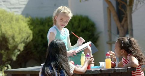 Children drawing together at outdoor picnic table