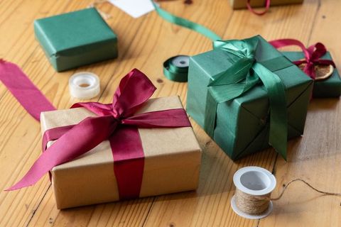 Handwrapped kraft gift with burgundy ribbon on wooden table with green presents, twine