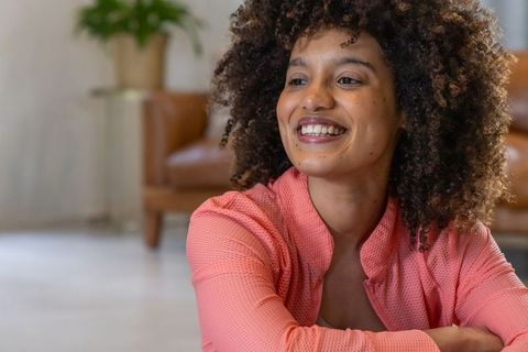 Smiling african american woman wearing coral zip top in cozy living room, natural light