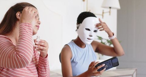 African american friends applying led mask and serum during at-home skincare session