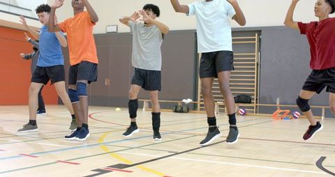 Diverse teen male volleyball team jumping during indoor drill with knee pads and training