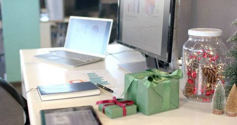Festive office desk showcasing wrapped gifts, jar of fairy lights and pinecone holiday decor
