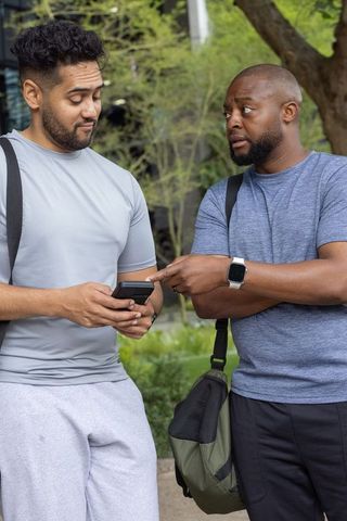 Two friends checking smartphone on campus walkway wearing sportswear and backpacks