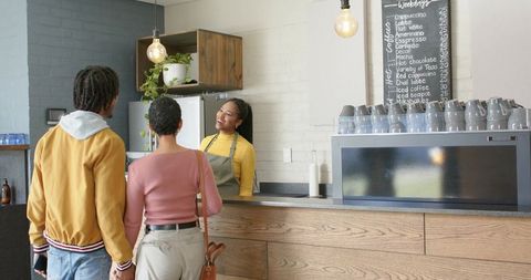 Couple holding hands at cafe counter while smiling barista leaning and chatting warmly