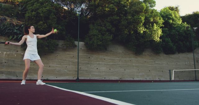 A young Caucasian woman is playing tennis on an outdoor court, with copy space. Her athletic stance and focus capture the intensity of the sport.