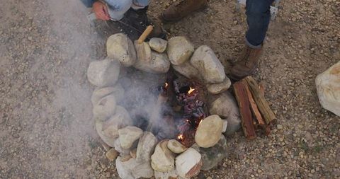 Overhead view friends stoking embers in stone fire ring on gravel campsite