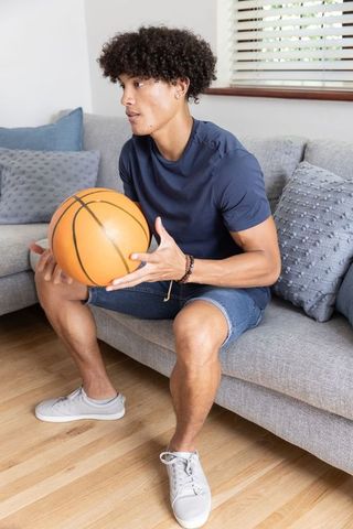Young man in denim shorts relaxing with basketball indoors