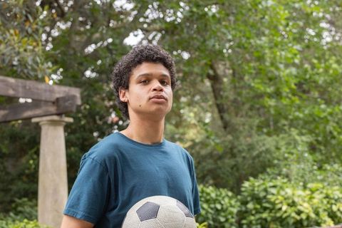 Young man standing in garden holding soccer ball near pergola and stone column