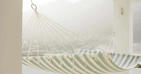 Striped cotton hammock hanging on white porch columns over hazy valley view calm retreat