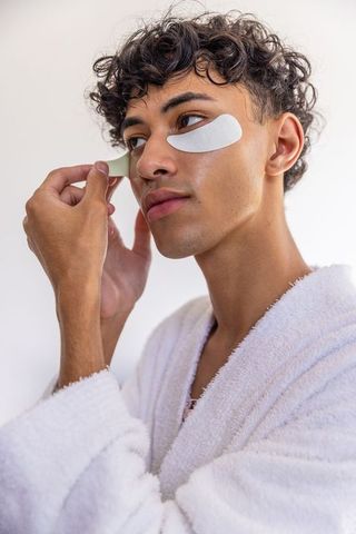 Man applying under-eye patches in bathroom routine