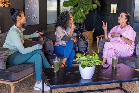 Multiracial women recording wellness podcast hosting panel discussion in cozy lounge