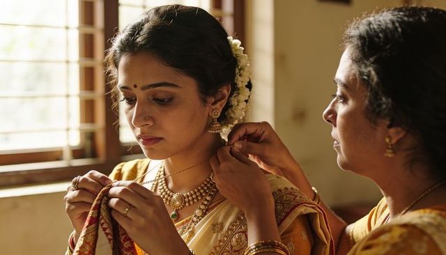 Mother fastening gold necklace on daughter wearing south indian saree and jasmine garland