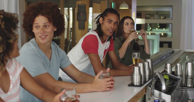 This image shows a diverse group of young adults sitting at a bar counter, enjoying drinks and engaging in conversation. Perfect for use in social media promotions, hospitality marketing, and articles about social life and nightlife.