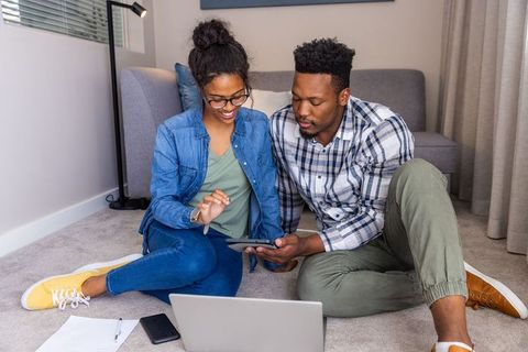 Young couple planning budget at home using tablet and laptop on living room floor