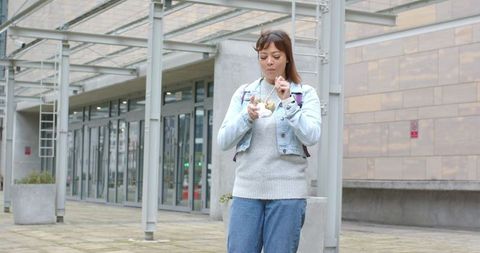 Mid 30s woman eating takeaway under modern pergola at urban plaza during lunch break
