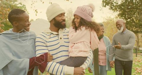Multigenerational family enjoying autumn park walk, father carrying daughter, warm smiles